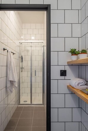 Ein modernes Badezimmer mit weißen Fliesen, einer Duschkabine aus Glas und einem Holzboden mit Handtüchern und Topfpflanzen.