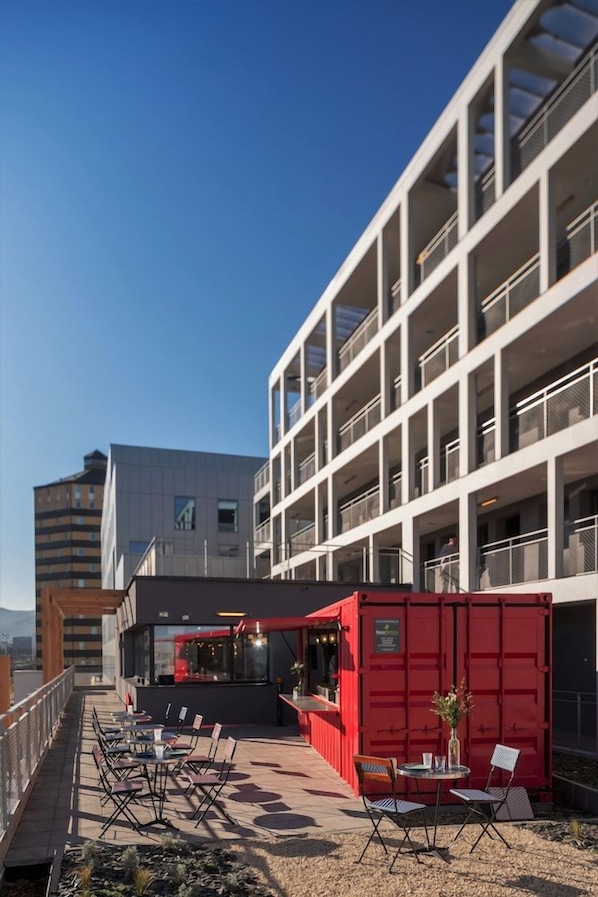 A rooftop terrace with outdoor seating, a red container, and a modern building in the background. - Eklo Clermont Ferrand Centre Gare (Clermont-Ferrand)