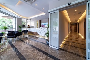 A modern hotel lobby with a marble reception desk, black upholstered chairs, and a glass partition. - Garden Room Suit Hotel (Istanbul)