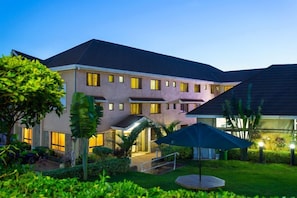 A multi-story hotel with a flat roof, a covered outdoor area with a blue umbrella, and well-maintained landscaping. - Phoenicia Hotel (Kiambu)