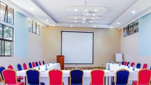 A conference room with a large screen, multiple tables, and chairs arranged for a meeting. - Phoenicia Hotel (Kiambu)