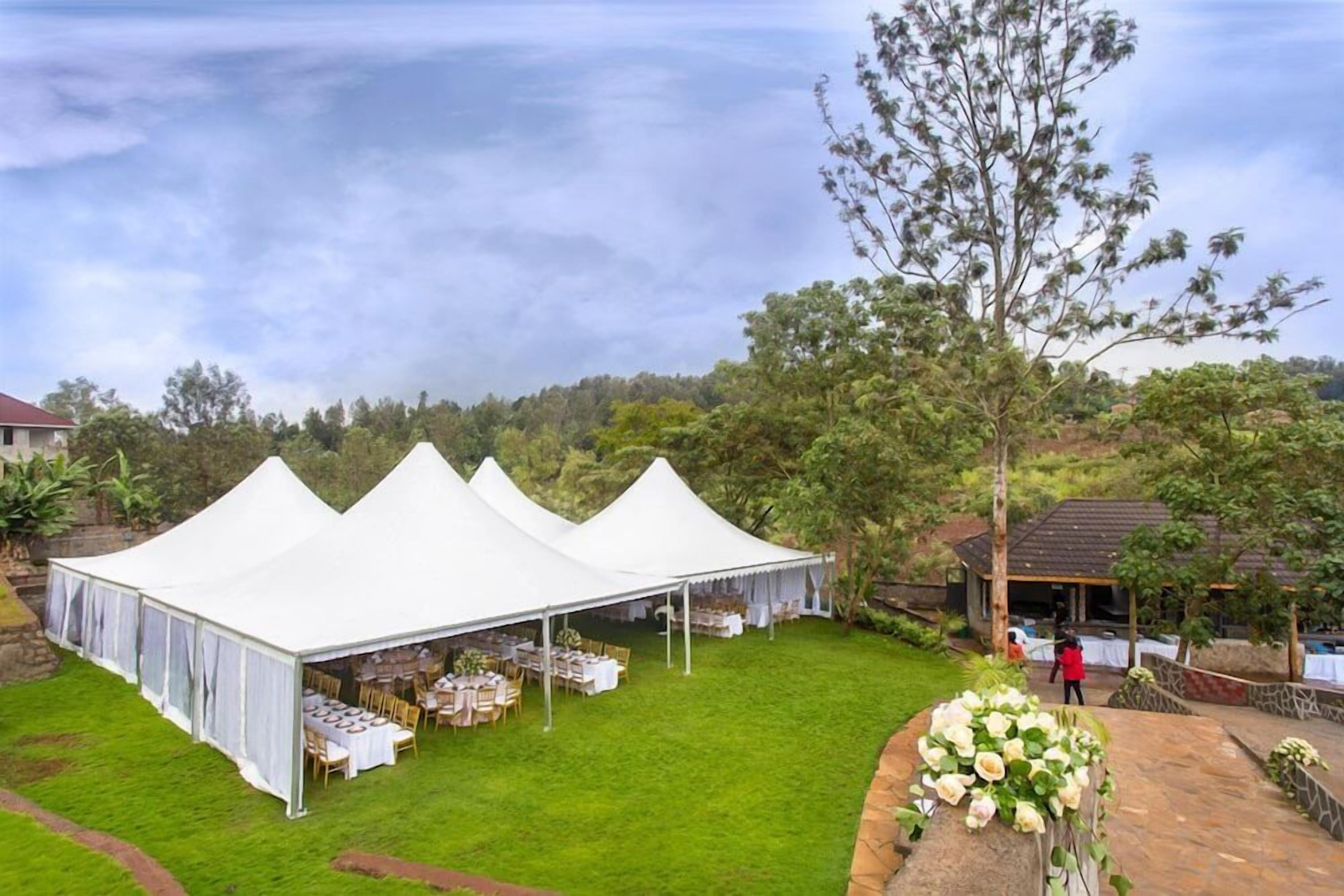 A tented outdoor event space with tables set up for dining, surrounded by greenery and trees.