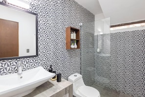 Un bagno con una parete a motivi geometrici, uno scaffale in legno con articoli da toilette, un lavandino bianco e un water.