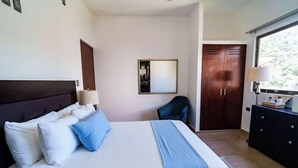 Quarto de hotel com cama, escrivaninha, cadeira, guarda-roupa e janela.