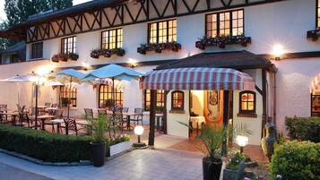 Il s’agit d’un bâtiment traditionnel doté d’un toit de chaume, de nombreuses fenêtres et d’un espace extérieur aménagé avec des tables et des parasols.