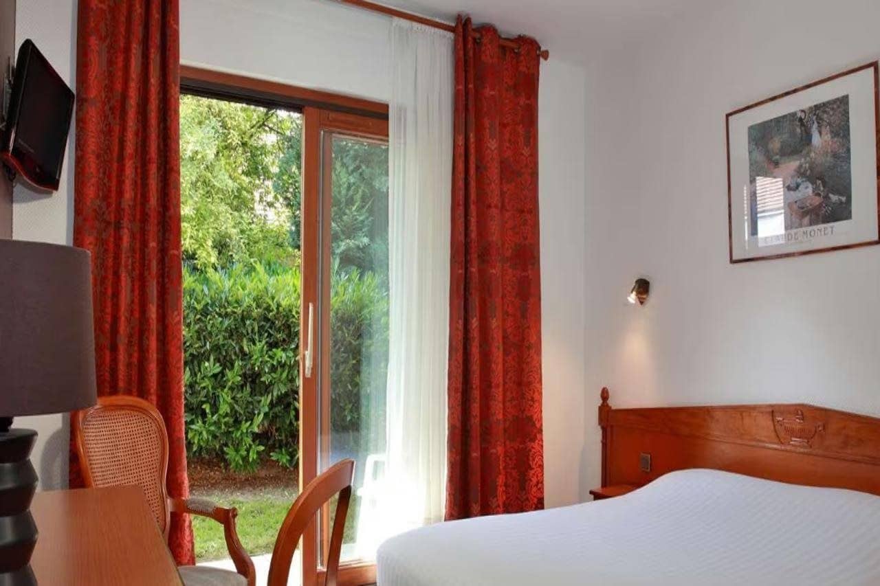 Une chambre d’hôtel équipée d’un lit, d’un bureau, d’une chaise, d’une télévision et d’une fenêtre avec des rideaux.