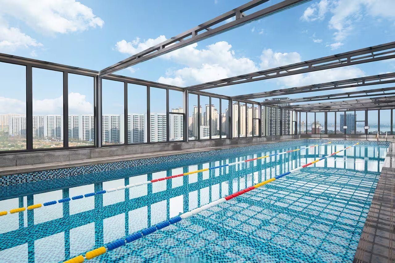 Une piscine intérieure avec des parois en verre transparent, un sol carrelé et une vue sur la ville.