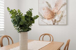A dining area with a wooden table, a woven plant pot, and a framed artwork on the wall. - New Farm Hideaway with Courtyard - 2Bed-1Bath-1Car (New Farm)