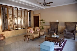 A living room with a sofa, armchairs, a coffee table, and a decorative screen. - Mastiff Hotel Palampur (Palampur)