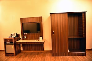 A room with a built-in TV, a wooden desk, a wardrobe, and a small refrigerator. - Mastiff Hotel Palampur (Palampur)