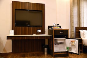 Habitación de hotel con televisor de pantalla plana en la pared, un refrigerador pequeño, una mesita de noche con lámpara y una cama con ropa blanca.