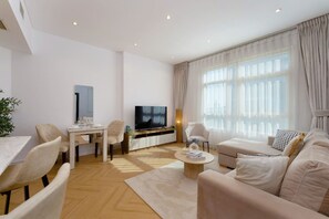 Uma sala de estar moderna com televisão de tela plana, área de jantar com mesa e cadeiras, e uma janela grande com cortinas.