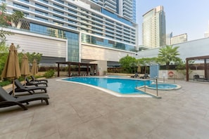 A rooftop swimming pool with lounge chairs and umbrellas, surrounded by modern buildings. - Sunny Marina Retreat - 1BR Near Metro station (Dubai)