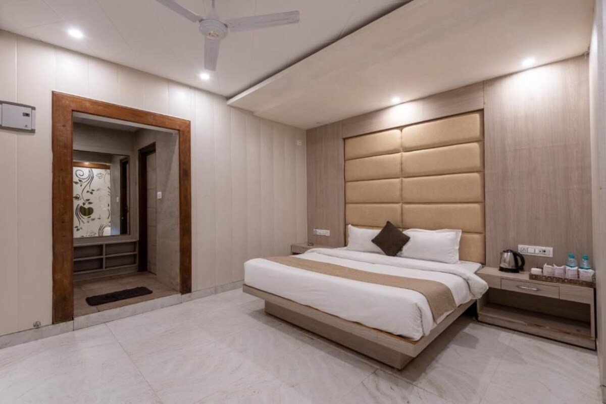 Una habitación de hotel moderna con una cama grande, una mesita de noche con hervidor y un ventilador de techo.