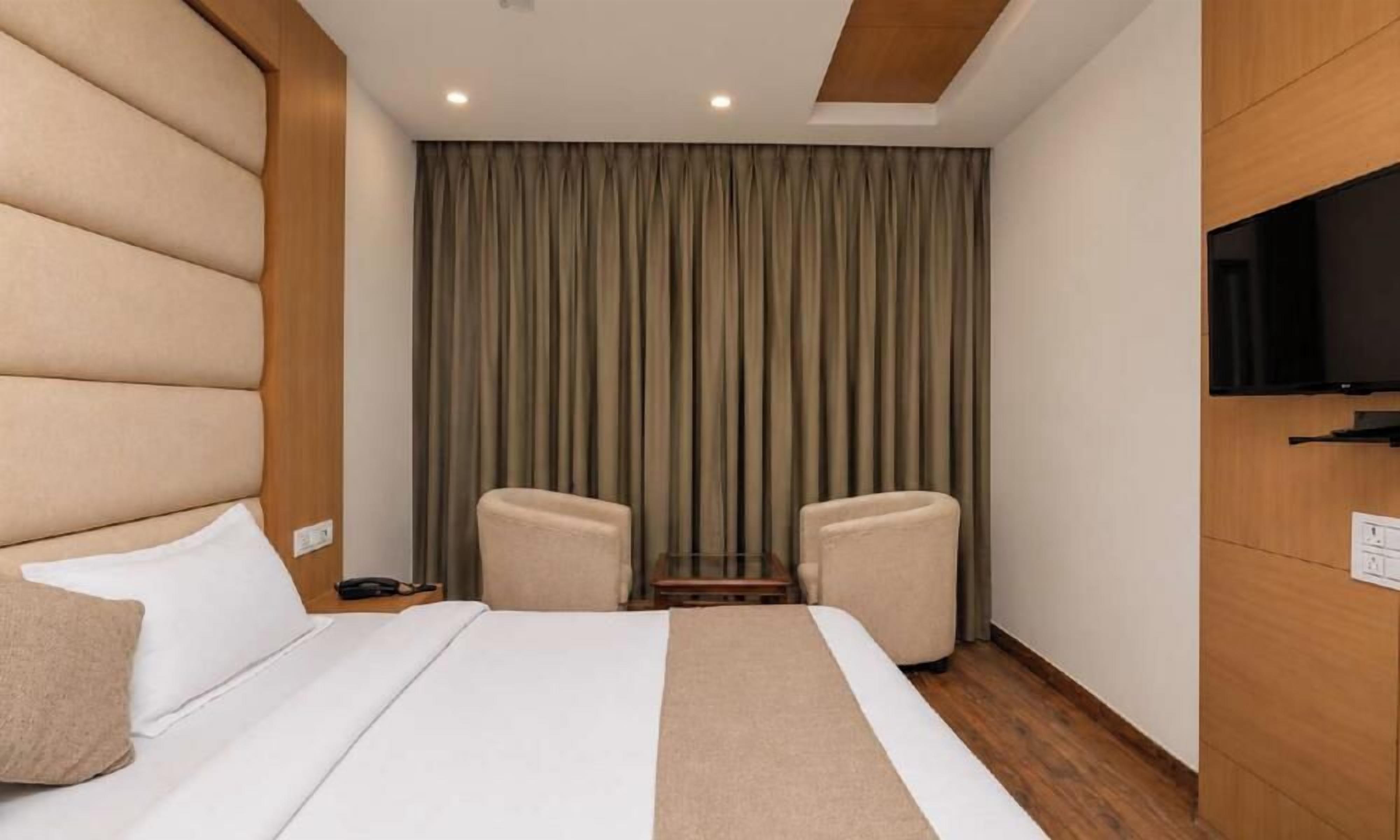 Habitación de hotel con una cama, dos sillones, un televisor y una cortina.
