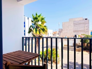 Un balcón con una mesa de madera, una palmera y vistas a edificios.