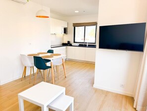 Moderni keittiö, jossa on valkoiset kaapit, musta työtaso ja seinälle asennettu litteänäyttöinen televisio.