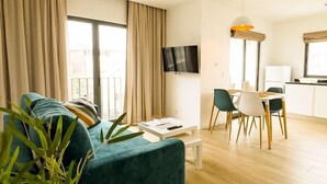En moderne stue med sofa, spisebord, stole, et fladskærms TV på væggen og en altan med gardiner.