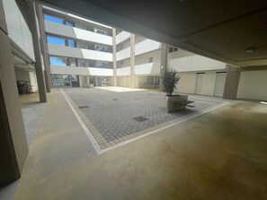 Ein geräumiger Innenhof mit Fliesenboden, einem zentralen Pflanzkübel und einem mehrstöckigen Gebäude im Hintergrund.