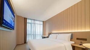Een hotelkamer met een bed, nachtkastje en een aan de muur bevestigde televisie.