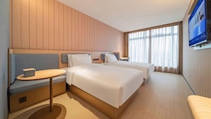 Een hotelkamer met twee bedden, een tafeltje, een televisie en een raam met gordijnen.