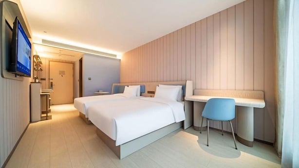 Een moderne hotelkamer met een groot bed, nachtkastjes, een bureau met stoel, een televisie en een badkamer in de achtergrond.