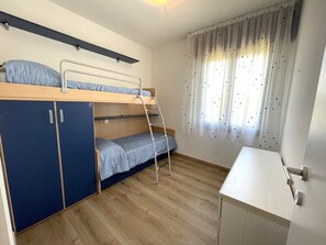 Ein Stockbett mit Schreibtisch und Kleiderschrank, ein Fenster mit Vorhängen und ein Holzboden.