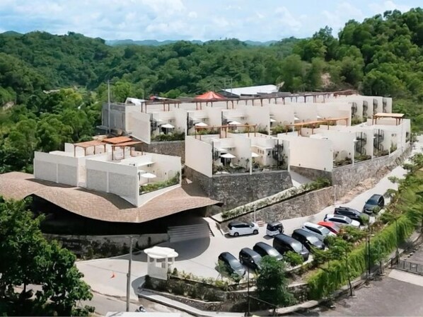 A modern hotel with multiple levels, a parking lot, and a view of the surrounding greenery. - Drini Park Resort (Wonosari)