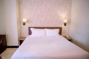 A hotel room with a large bed, two bedside lamps, a nightstand with a phone, and a patterned wall.