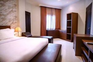 A hotel room with a large bed, a desk, a chair, a wardrobe, and a window with curtains.