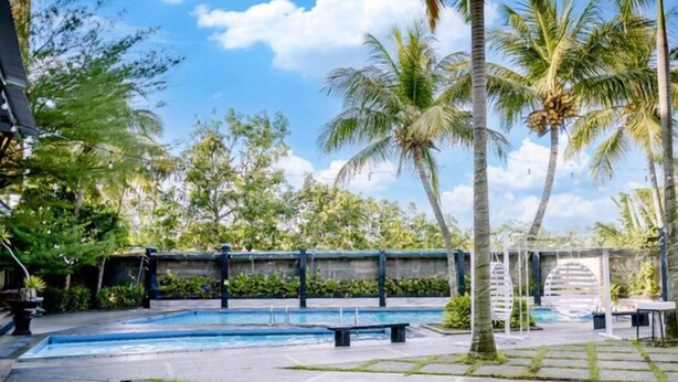 A swimming pool area with a stone deck, palm trees, and a covered seating area. - Smart Hotel (Lubuklinggau)