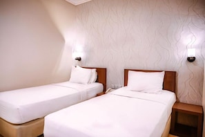 Habitación de hotel con dos camas individuales, cabecera de madera, mesita de noche y lámpara fijada a la pared.
