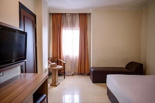 A hotel room with a flat-screen TV, a desk, a chair, a sofa, and a bed.