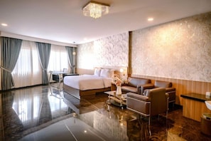 A hotel room with a bed, a seating area with a sofa and armchairs, a desk, and a large mirror. - Smart Hotel (Lubuklinggau)
