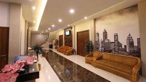 Een hotel lobby met een receptiebalie, twee banken, een stadsgezicht muurschildering en een trap.