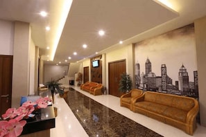 Rebedor d'hotel amb taulell de recepció, dos sofàs, mural de paisatge urbà i una escala.