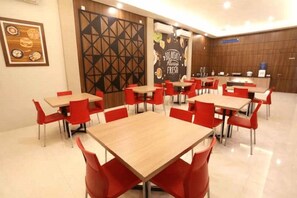 Un comedor con varias mesas y sillas rojas, una zona de cocina y una pared con un diseño geométrico y un cartel.