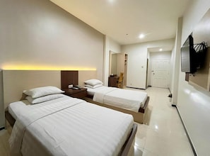 Habitación de hotel con dos camas, un escritorio, una silla, un televisor y una puerta que da a otra habitación.