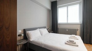 Habitación de hotel con una cama grande, lámparas de noche, una ventana con cortinas y un radiador.