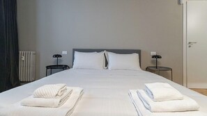 Habitación de hotel con una cama grande, dos mesitas de noche, un radiador y una puerta.