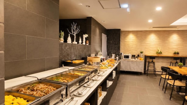 A buffet setup with multiple food stations, a seating area with tables and chairs, and a decorative wall with a tree sculpture. - Hotel Arashi Nambaminami No003 (Osaka)