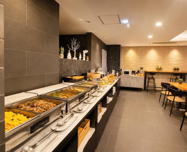 A buffet setup with multiple food stations, a seating area with tables and chairs, and a decorative wall with a tree sculpture. - Hotel Arashi Nambaminami No003 (Osaka)