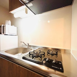 A modern kitchen with a stainless steel gas stove, a sink, and wooden cabinets. - Hotel Arashi Nambaminami No003 (Osaka)