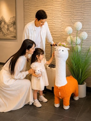 Una família interactua amb una estàtua d'un llama blanc i taronja en una habitació amb un mur amb textura i una planta en test.
