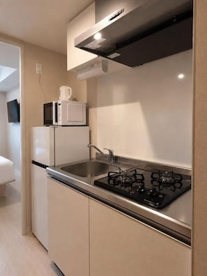 A compact kitchen with a gas stove, a microwave, and a sink. - Hotel Arashi Nambaminami No003 (Osaka)