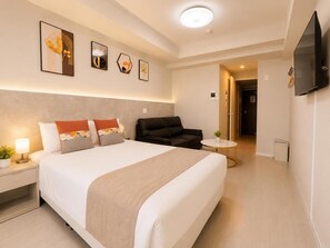 Habitació d'hotel moderna amb un llit gran, un sofà, una taula petita i un televisor de pantalla plana fixat a la paret.