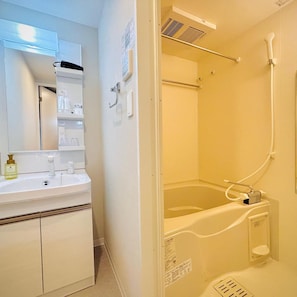 A bathroom with a white sink, mirror, and a bathtub with a showerhead. - Hotel Arashi Nambaminami No003 (Osaka)