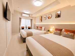 Habitació d'hotel amb dos llits, un televisor de pantalla plana fixat a la paret, una taula petita amb cadires i una finestra amb cortines.