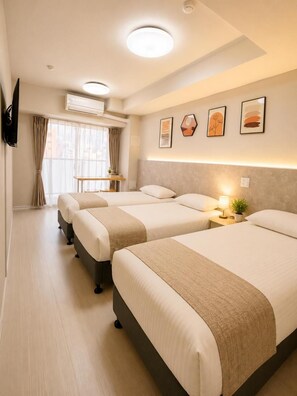 Habitación de hotel con tres camas, un televisor de pantalla plana montado en la pared, aire acondicionado y una ventana con cortinas.
