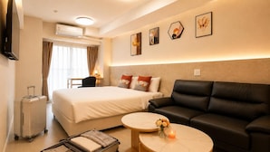 A hotel room with a bed, a black leather sofa, two round tables, a wall-mounted TV, and an air conditioning unit. - Hotel Arashi Nambaminami No003 (Osaka)